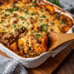 A casserole dish filled with roasted sweet potatoes, seasoned ground turkey, bell peppers, and melted cheese, garnished with fresh herbs.