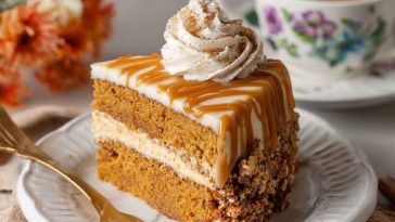 A slice of pumpkin spice latte cake topped with whipped cream and a dusting of cinnamon, served on a rustic fall-themed plate.