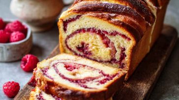 A golden raspberry swirl brioche loaf sliced to reveal its soft, buttery layers and vibrant raspberry filling.
