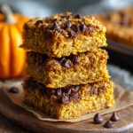 A tray of healthy pumpkin oatmeal bars cut into squares, topped with oats and cinnamon, served on a rustic wooden board.