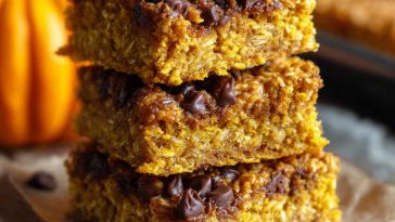 A tray of healthy pumpkin oatmeal bars cut into squares, topped with oats and cinnamon, served on a rustic wooden board.