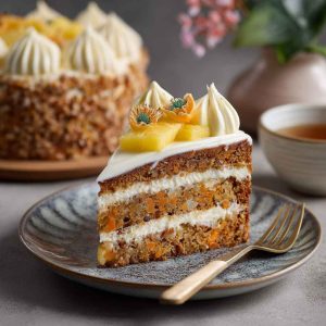 Moist pineapple carrot cream cake topped with whipped cream cheese frosting and garnished with crushed pineapple and shredded carrots.