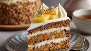 Moist pineapple carrot cream cake topped with whipped cream cheese frosting and garnished with crushed pineapple and shredded carrots.