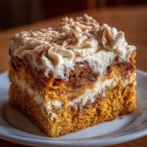 Moist pumpkin spice gooey cake topped with rich cream cheese frosting, dusted with cinnamon and served in warm autumn lighting.