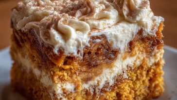 Moist pumpkin spice gooey cake topped with rich cream cheese frosting, dusted with cinnamon and served in warm autumn lighting.