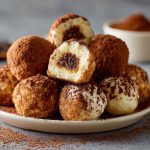 Tiramisu truffles dusted with cocoa powder and arranged on a plate with coffee beans and chocolate shavings.
