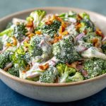 Creamy broccoli ranch salad with bacon, cheddar, and sunflower seeds in a white bowl.