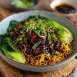 Sticky beef noodles tossed in a glossy soy-based sauce, garnished with sesame seeds and green onions in a ceramic bowl.