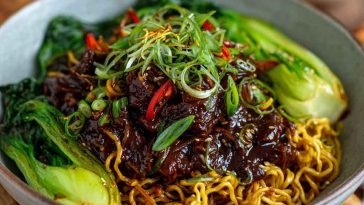 Sticky beef noodles tossed in a glossy soy-based sauce, garnished with sesame seeds and green onions in a ceramic bowl.