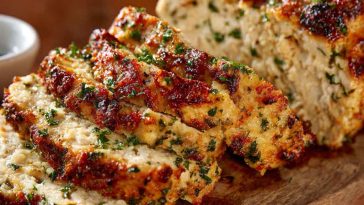 Chicken meatloaf with garlic parmesan flavor, sliced and served with fresh herbs on a rustic cutting board, golden crust and juicy interior visible.
