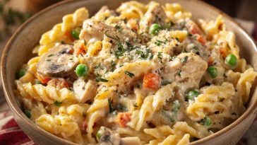 A creamy bowl of chicken pot pie pasta filled with tender rotini, shredded chicken, peas, carrots, and a rich, savory sauce, garnished with fresh parsley.