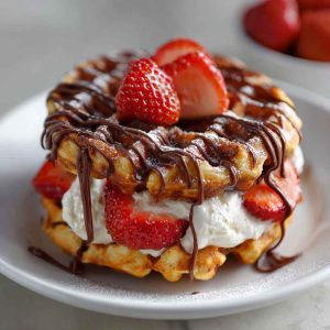 Golden donut-shaped chaffles dusted with cinnamon and served with a sugar-free glaze on a plate.