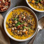 Bowl of creamy pumpkin wild rice soup garnished with herbs and served with crusty bread.