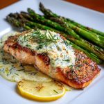 Baked salmon fillet topped with melted Boursin cheese and fresh herbs on a white plate.
