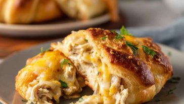 Golden-baked crescent rolls stuffed with creamy shredded chicken and melted cheese, served on a white plate with a sprinkle of parsley.