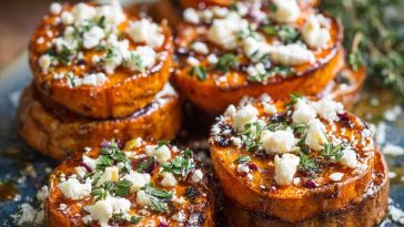 Golden roasted sweet potato rounds topped with crumbled feta, a drizzle of honey, and fresh thyme on a serving platter.