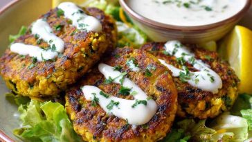 Golden chickpea patties with lemon zest served with creamy yogurt sauce and fresh herbs on a plate.