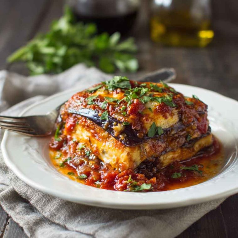 A slice of eggplant lasagna layered with roasted eggplant, marinara sauce, melted mozzarella, and fresh basil on a rustic plate.