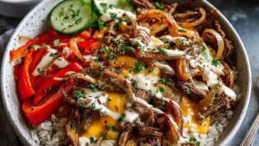 Deconstructed Philly cheesesteak bowl with sliced steak, sautéed peppers and onions, melted provolone, and roasted potatoes served in a rustic bowl.