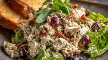 A vibrant bowl of Italian grinder chicken salad with shredded lettuce, grilled chicken, salami, cherry tomatoes, red onion, pepperoncini, and creamy dressing.