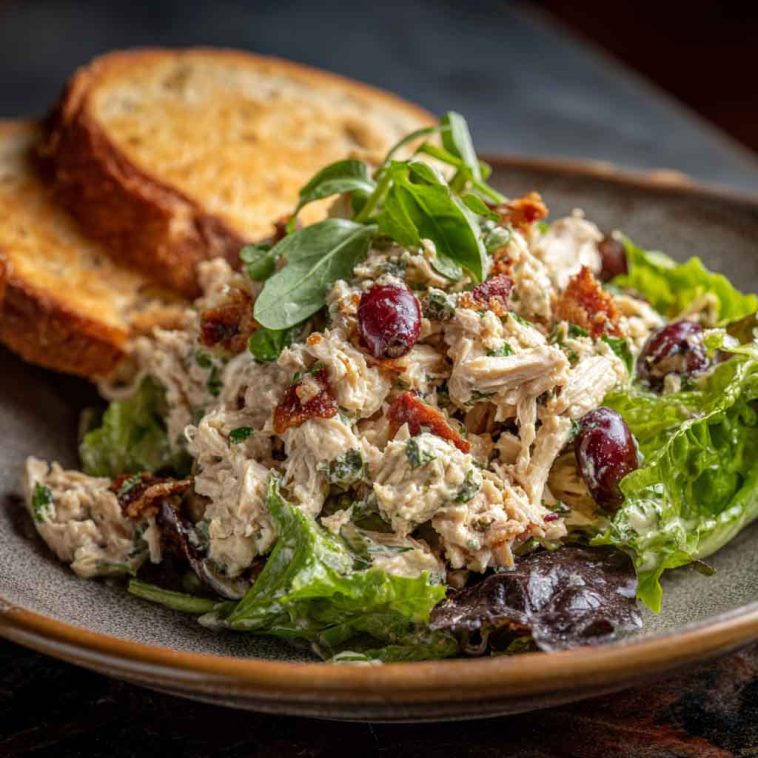 A vibrant bowl of Italian grinder chicken salad with shredded lettuce, grilled chicken, salami, cherry tomatoes, red onion, pepperoncini, and creamy dressing.