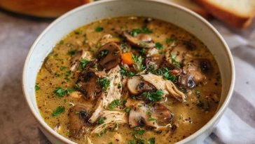 A bowl of creamy rotisserie chicken and mushroom soup garnished with fresh thyme and cracked black pepper, served with crusty bread on the side.