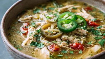 Green enchilada chicken soup served in a bowl with shredded chicken, green chilies, corn, and creamy broth, topped with cilantro, avocado slices, and shredded cheese.