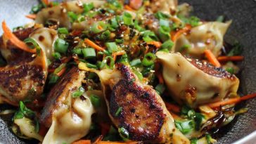 A colorful stir fry with crispy potstickers, sautéed vegetables, and a savory glaze, served in a wok and garnished with sesame seeds and green onions.