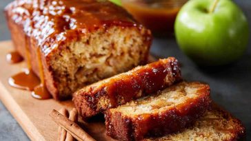 A golden-brown apple butter loaf sliced to reveal a moist, spiced interior, topped with a drizzle of glaze and a sprinkle of cinnamon.
