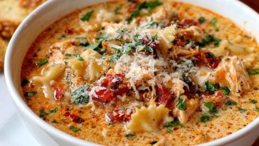 Creamy chicken parmesan soup in a bowl topped with melted cheese, herbs, and shredded chicken.