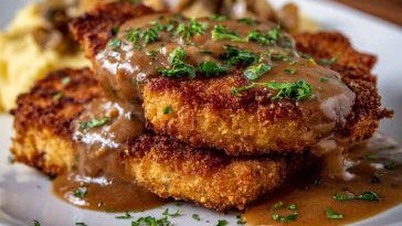 Golden, crispy country fried pork chops smothered in creamy gravy, served with mashed potatoes and green beans on a rustic plate.