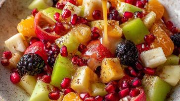 A vibrant bowl of winter fruit salad featuring pomegranate seeds, citrus slices, apples, and pears, drizzled with cinnamon vanilla dressing.