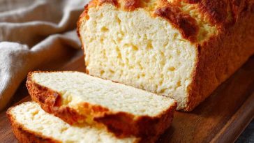 A loaf of zero carb yogurt bread sliced on a wooden board, showing its fluffy texture and golden crust.