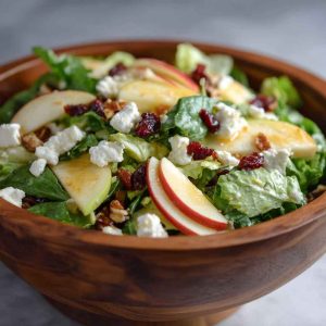 Honeycrisp apple and feta salad with mixed greens, cranberries, and walnuts in a white bowl.