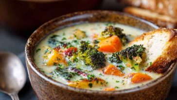 A rustic pot of creamy vegetable soup filled with carrots, potatoes, peas, and herbs, garnished with fresh parsley.