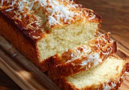 Moist coconut loaf cake topped with shredded coconut, sliced and served on a tropical-inspired platter.