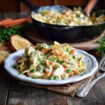 Creamy chicken pot pie pasta with vegetables and herbs in a skillet, garnished with fresh parsley.