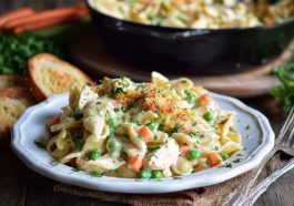Creamy chicken pot pie pasta with vegetables and herbs in a skillet, garnished with fresh parsley.