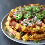 Golden cornbread waffles with melted cheddar and jalapeño slices, topped with sour cream and fresh cilantro.