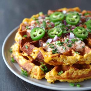 Golden cornbread waffles with melted cheddar and jalapeño slices, topped with sour cream and fresh cilantro.
