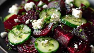 A vibrant beet salad with diced roasted beets, sliced cucumbers, crumbled feta cheese, and fresh herbs, drizzled with olive oil.