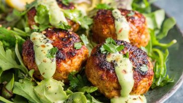 Salmon meatballs drizzled with creamy avocado sauce, served with fresh herbs and lemon wedges.