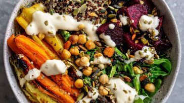 Colorful plant-based bowl filled with roasted vegetables, grains, greens, and drizzled with creamy tahini yogurt sauce.