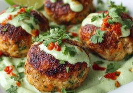 Golden salmon balls served with a swirl of creamy avocado sauce, garnished with fresh herbs and lime wedges.