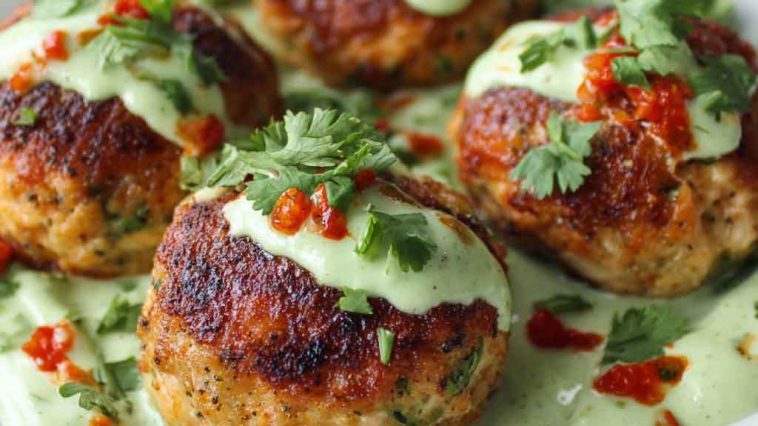 Golden salmon balls served with a swirl of creamy avocado sauce, garnished with fresh herbs and lime wedges.