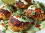 Golden salmon balls served with a swirl of creamy avocado sauce, garnished with fresh herbs and lime wedges.