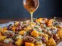 A rustic sheet pan filled with golden gnocchi, roasted butternut squash cubes, spicy sausage slices, and a drizzle of hot honey, garnished with fresh herbs.