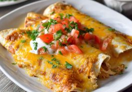 A baking dish filled with golden chicken enchiladas smothered in creamy queso sauce, topped with melted cheese and fresh cilantro.