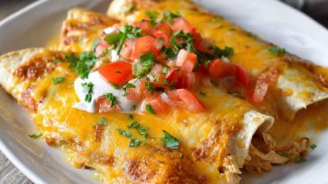 A baking dish filled with golden chicken enchiladas smothered in creamy queso sauce, topped with melted cheese and fresh cilantro.