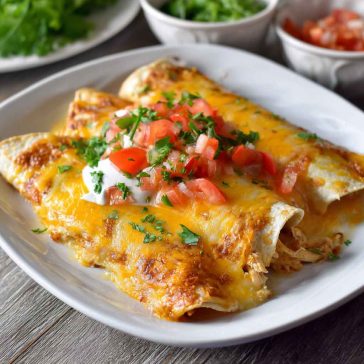 A baking dish filled with golden chicken enchiladas smothered in creamy queso sauce, topped with melted cheese and fresh cilantro.